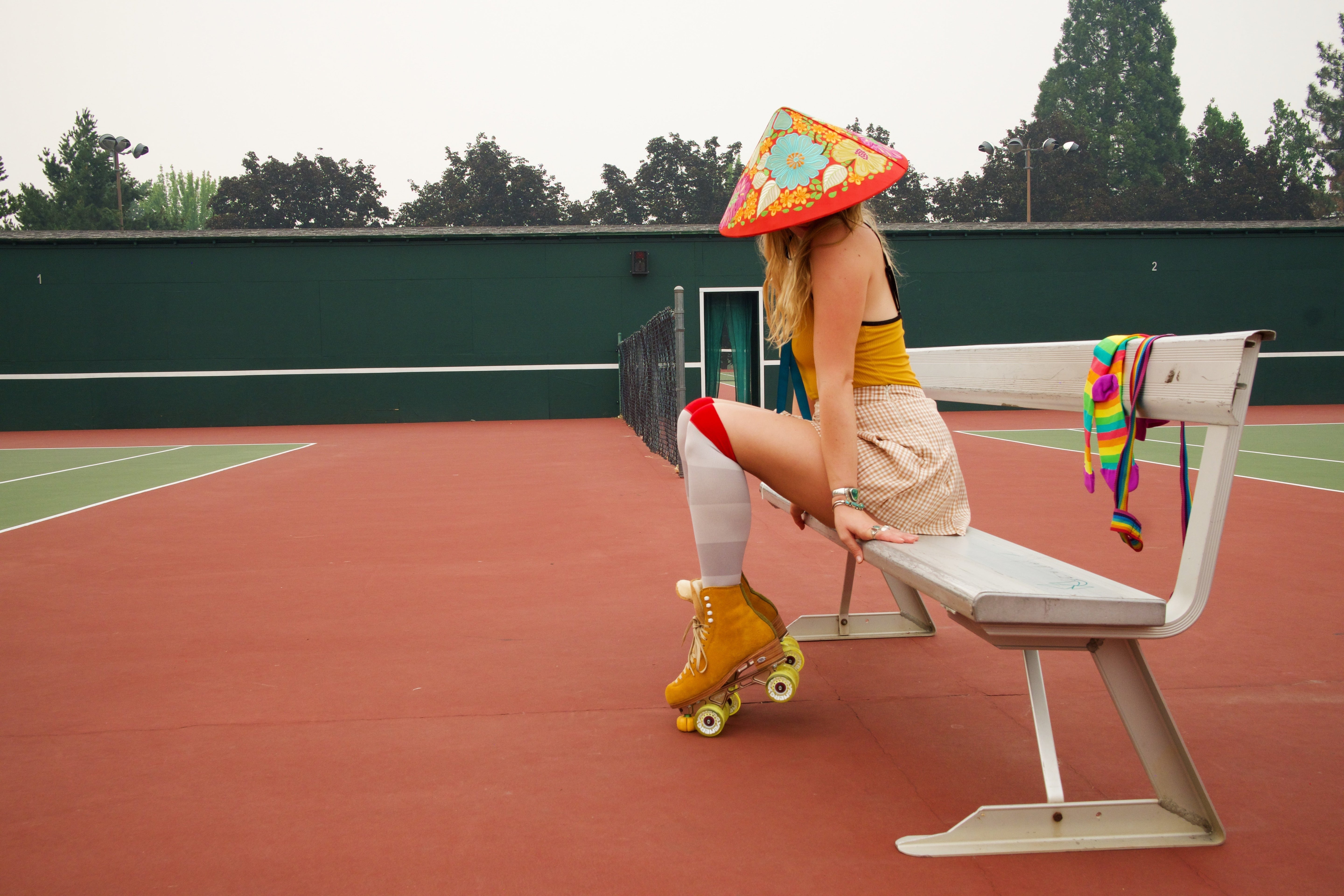 compression socks on a beautiful woman sitting on a bench in a tennis court wearing a pointy hat and roller skates