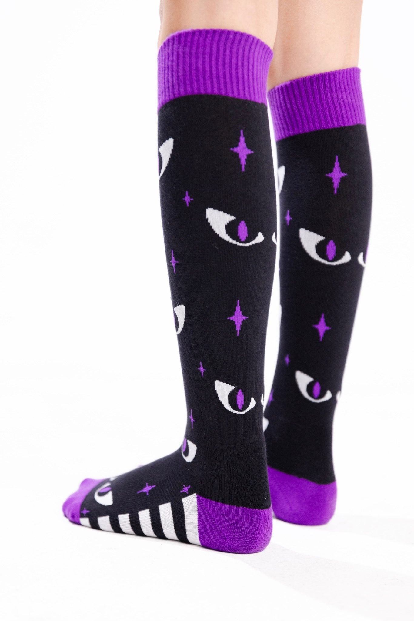 Black knee-high socks with purple cuffs, toes and heels, featuring white cat eyes with purple pupils, purple stars, and black-and-white stripes along the feet.