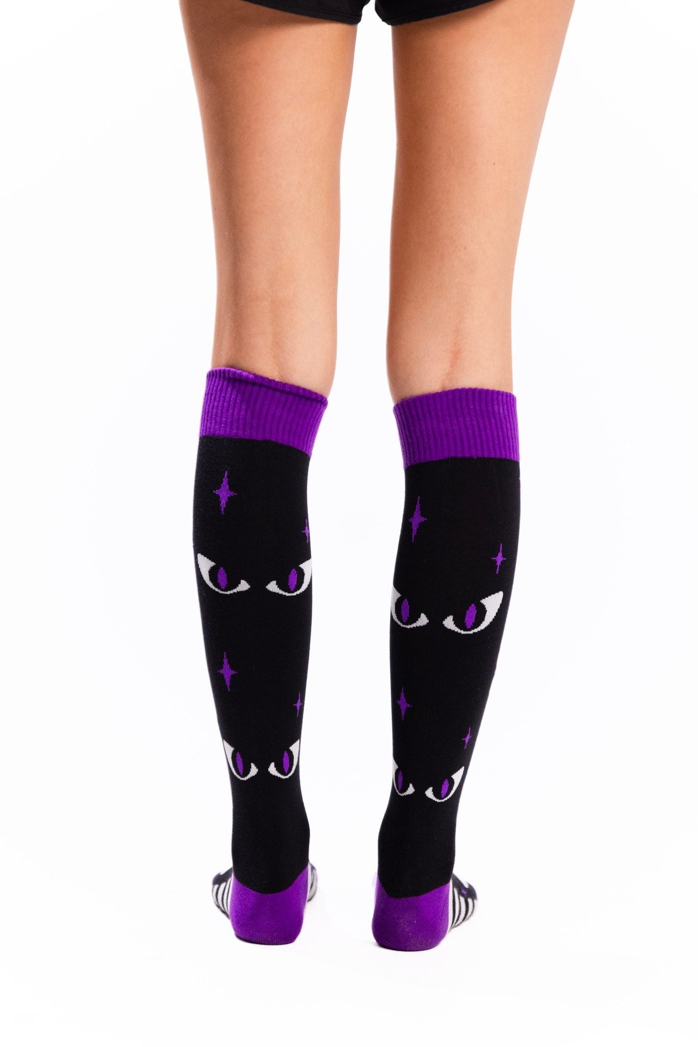 Black knee-high socks with purple cuffs, toes and heels, featuring white cat eyes with purple pupils, purple stars, and black-and-white stripes along the feet.