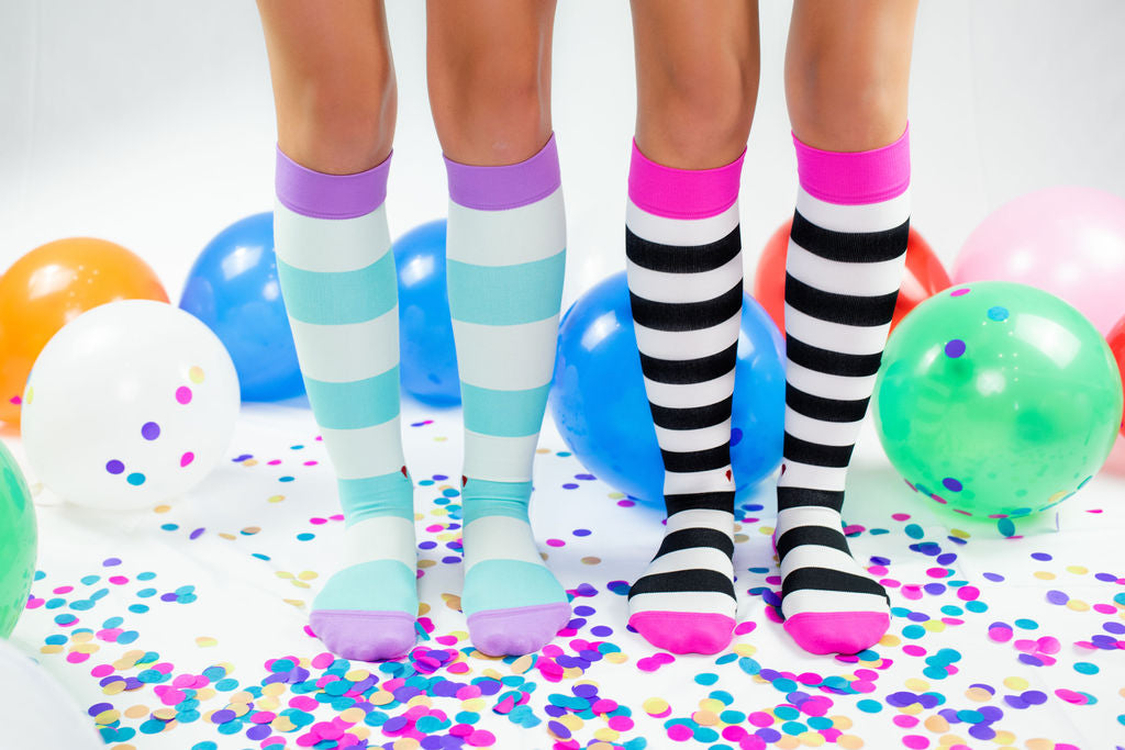 compression socks in aqua stripes with lavender purple accents and compression socks in black and white stripes with hot pink accents surrounded by multicolored confetti and balloons