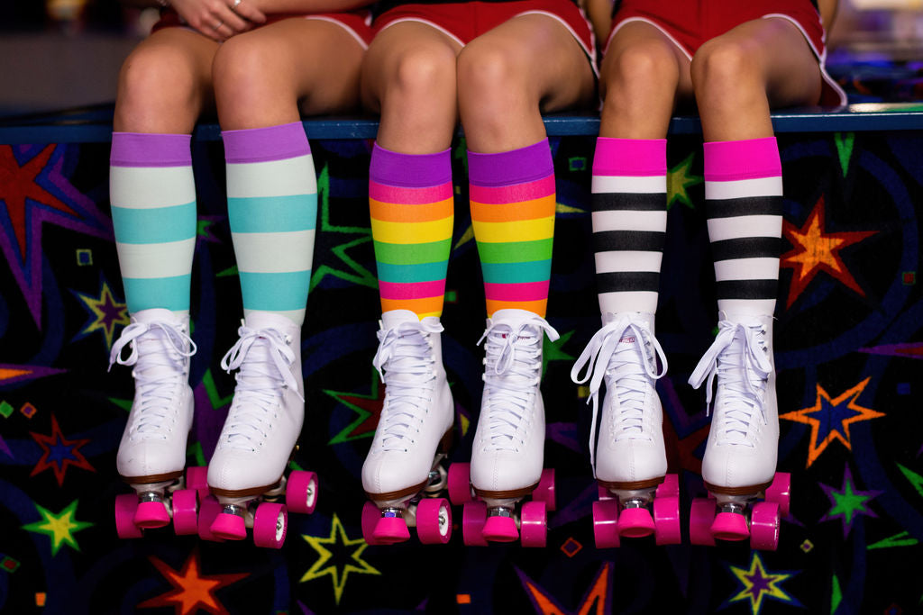 compression socks with rainbow stripes in pink, orange, yellow, green, and teal with purple accents worn by a roller skater