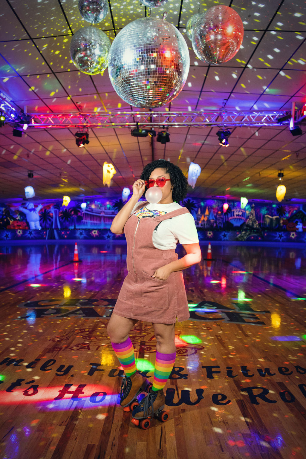 compression socks with rainbow stripes in pink, orange, yellow, green, and teal with purple accents worn by a roller skater in a roller rink under disco balls