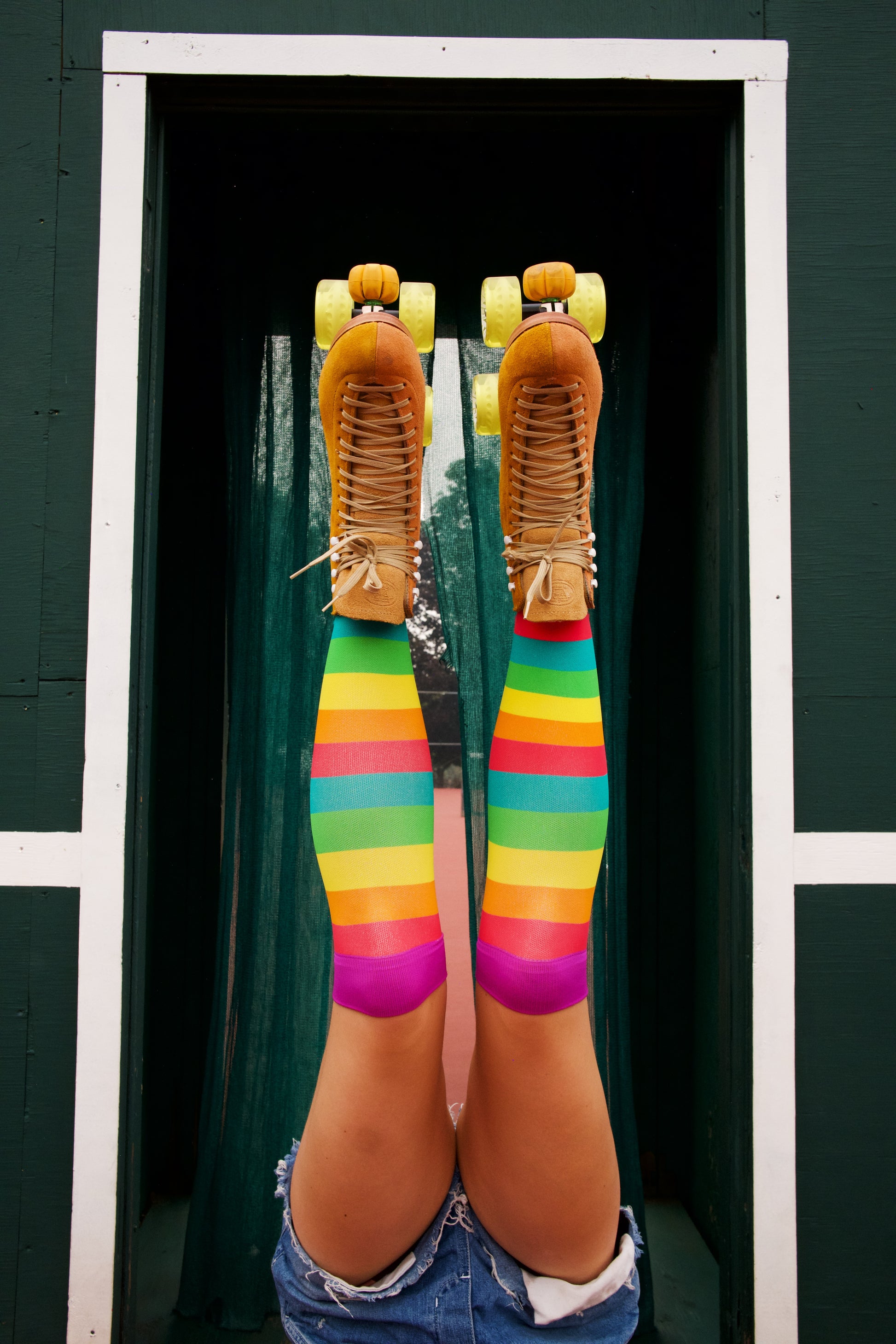 compression socks with rainbow stripes in pink, orange, yellow, green, and teal with purple accents- worn with roller skates and denim shorts
