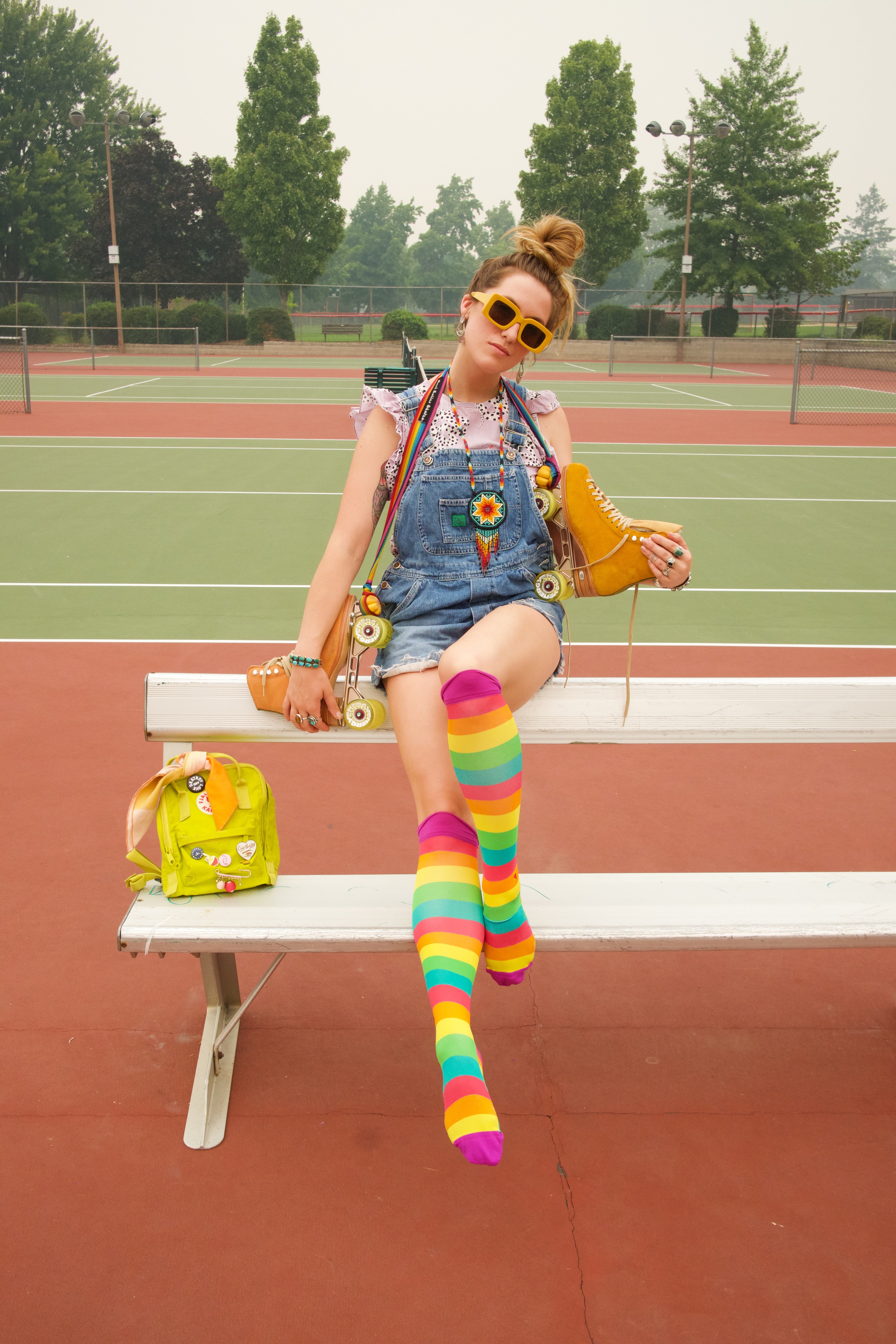 compression socks with rainbow stripes in pink, orange, yellow, green, and teal with purple accents worn by a roller skater on a tennis court