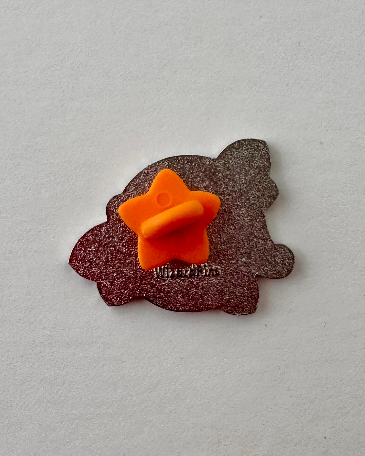 Colorful enamel pin with 'Ruby' text on a grapefruit background, the back showing an orange star rubber clasp