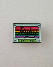 Colorful cassette tape-shaped enamel pin with 'Ruby' branding on a rainbow stripe