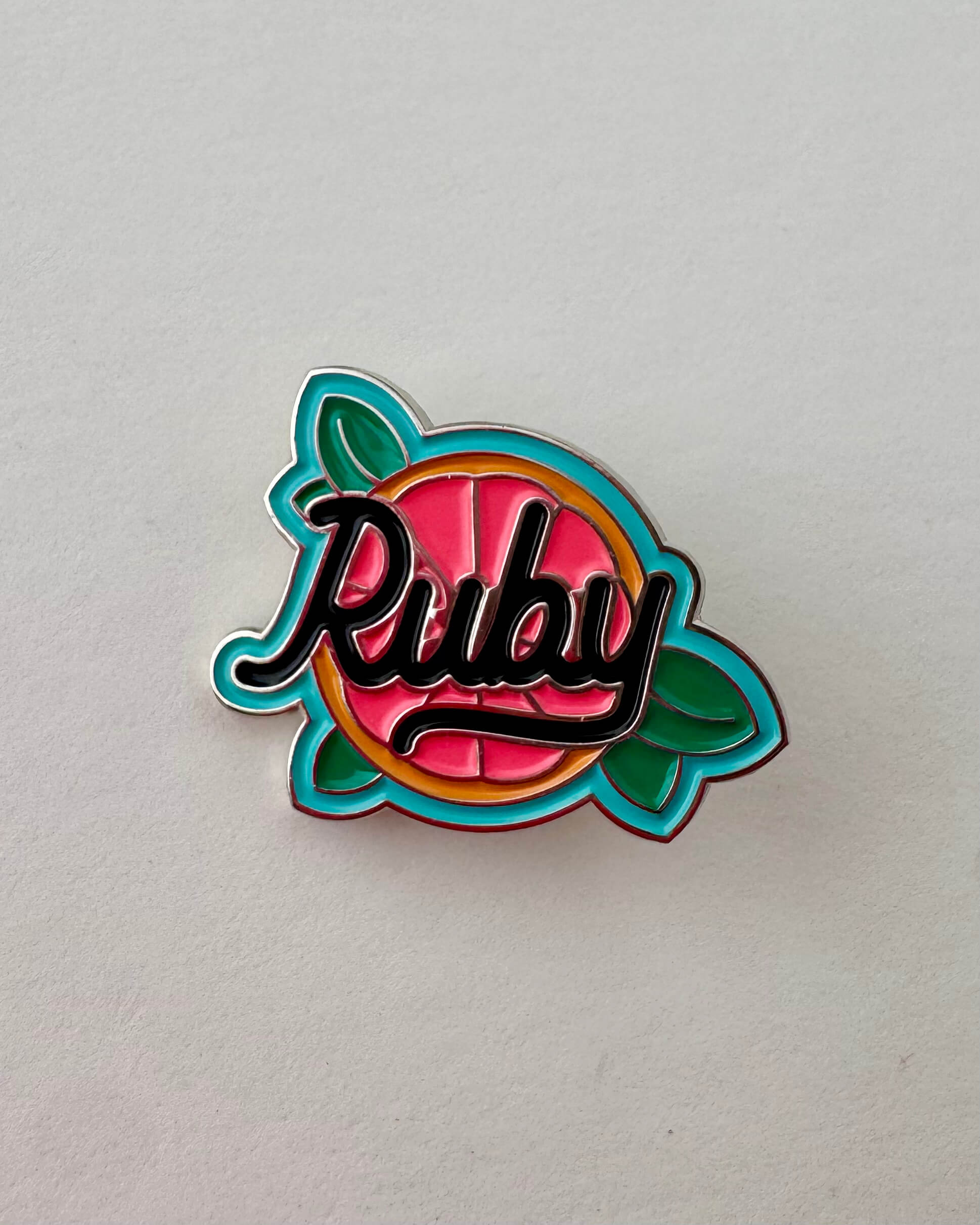 Colorful enamel pin with 'Ruby' text on a grapefruit background