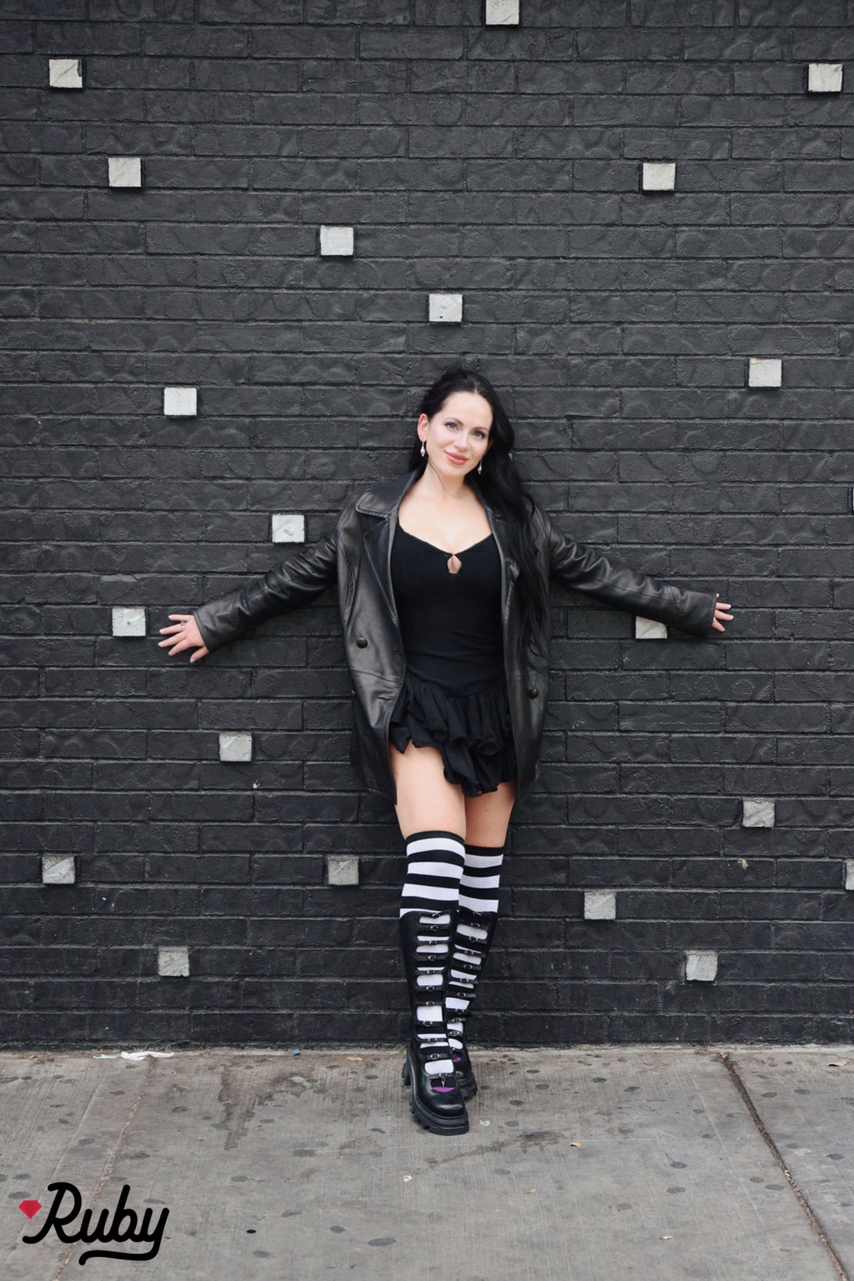 Model wearing Sabrina black and white striped thigh high socks with a black outfit and tall black boots.